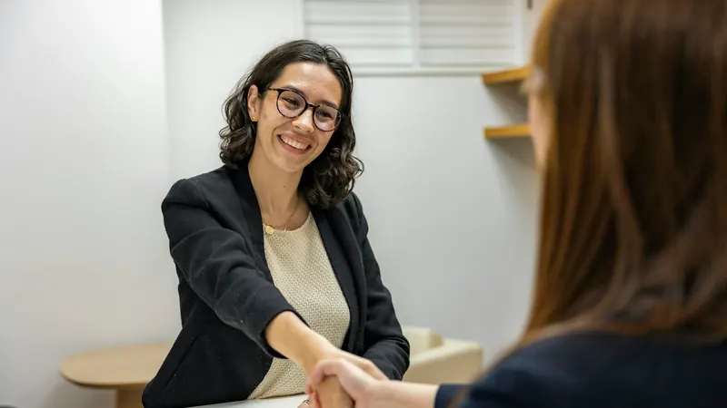 Two people greeting each other across a desk before an interview